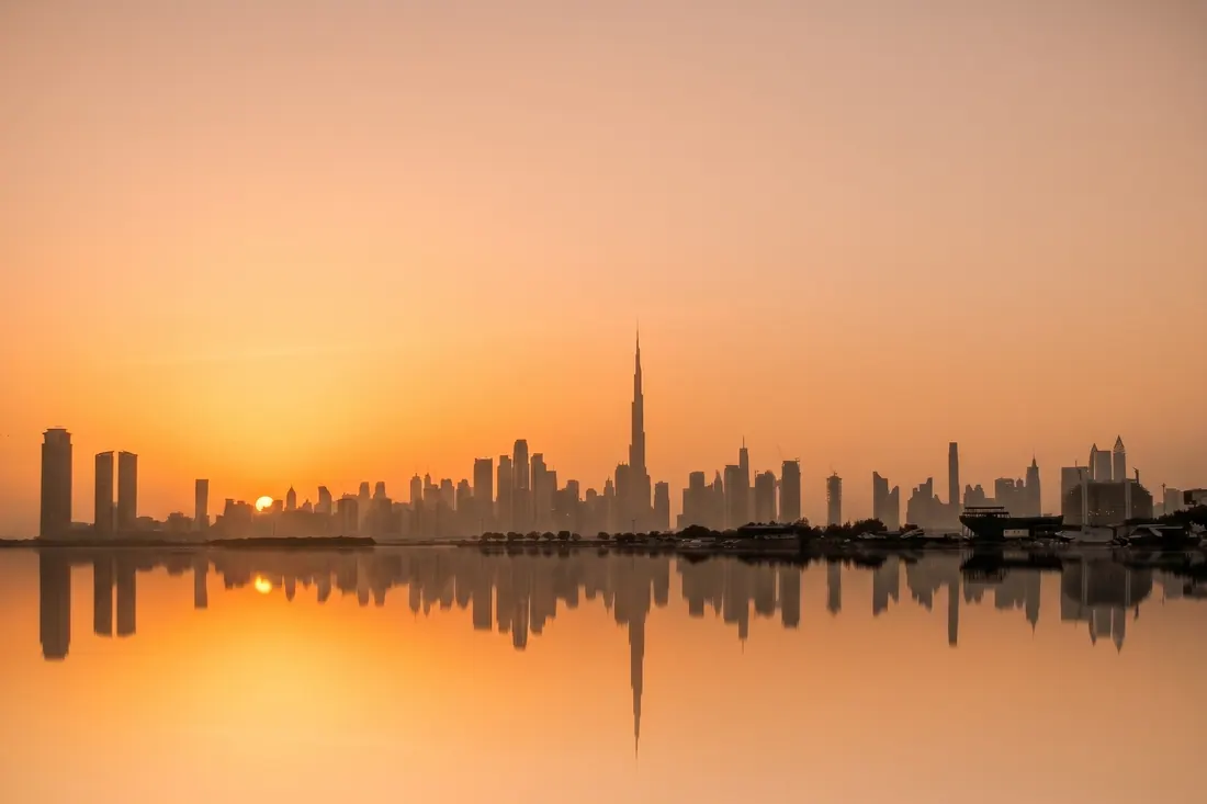 The Dubai skyline at sunrise, mirrored in still water.
