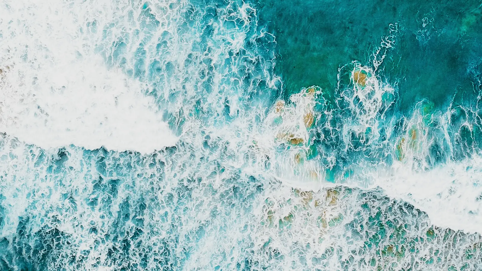 Turquoise surf meeting red sand, seen from directly above.