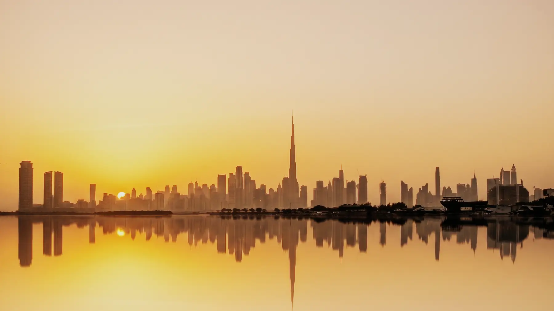 The Dubai skyline and the Burj Khalifa at sunset, reflected in the water.