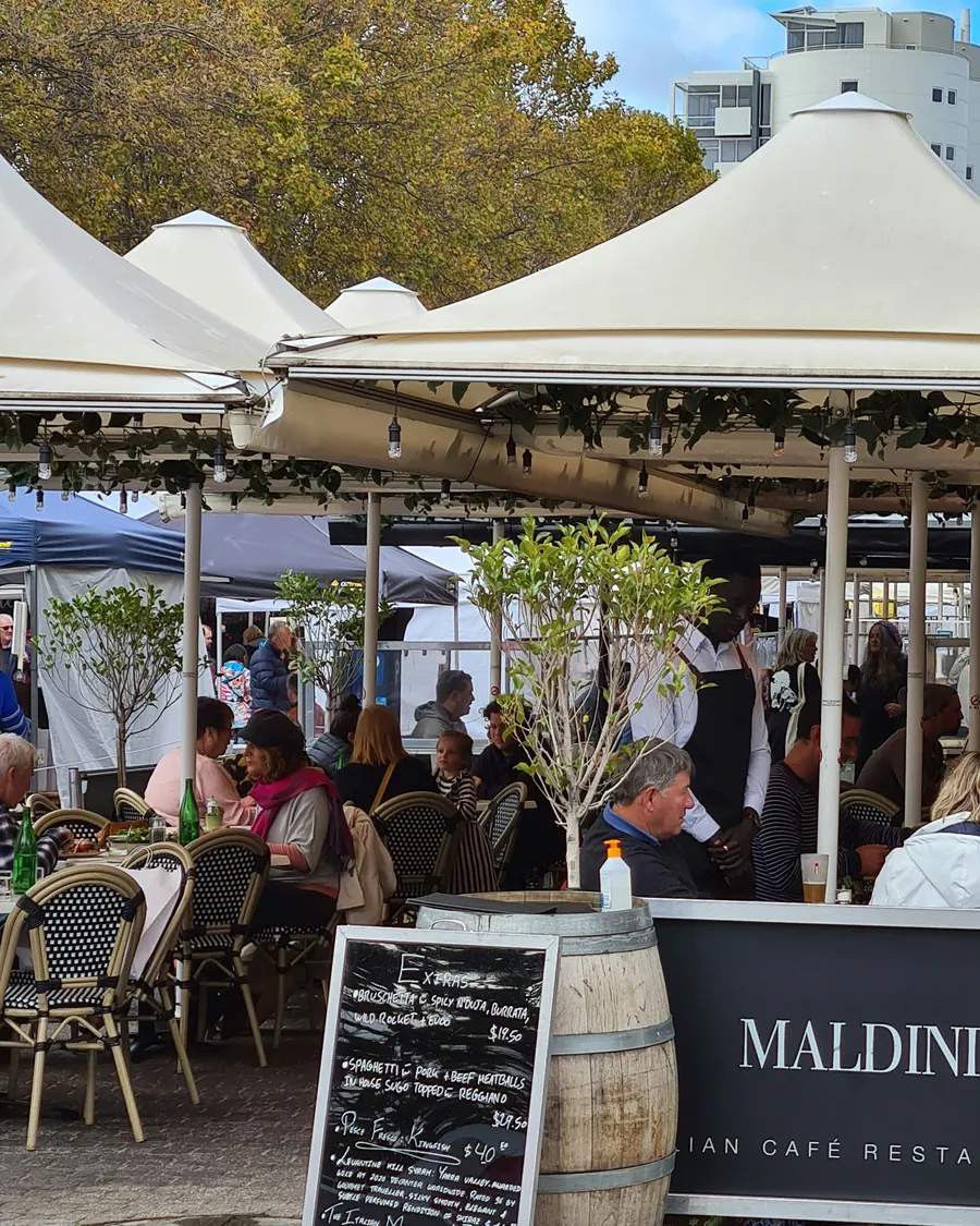 People eating at an outdoor café under white umbrellas on Salamanca Place, Hobart.