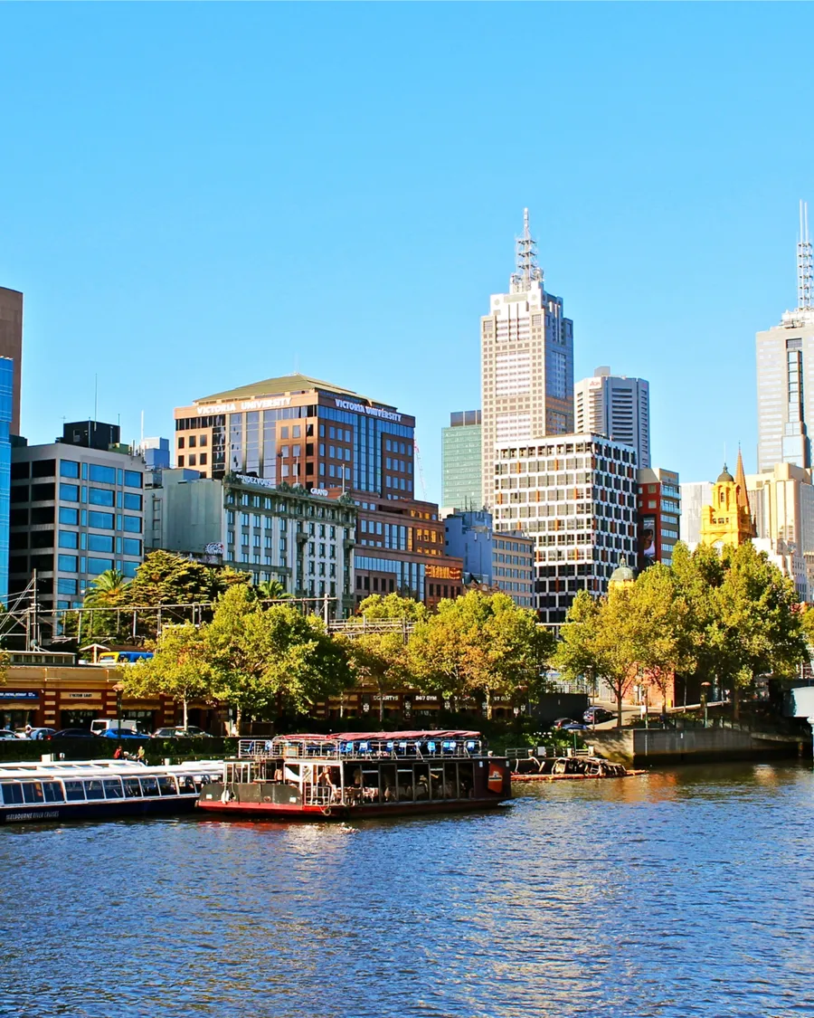 The Melbourne skyline across the Yarra River, with river boats moored on the bank.