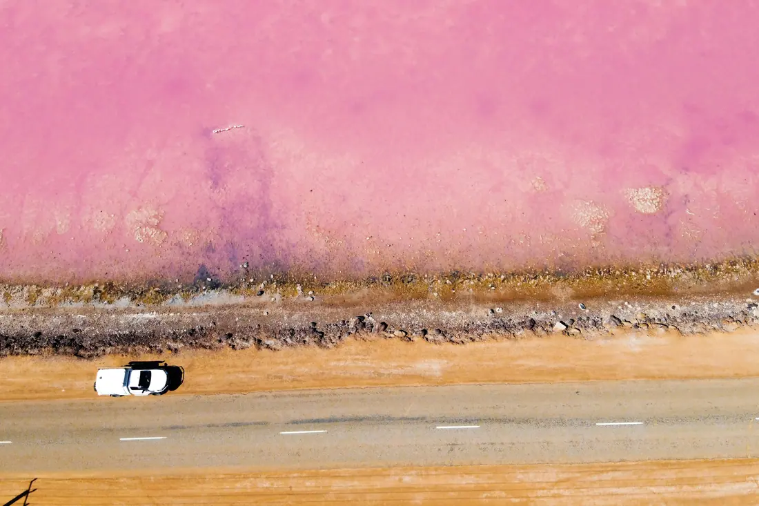 A road beside a pink salt lake in Western Australia, seen from above.