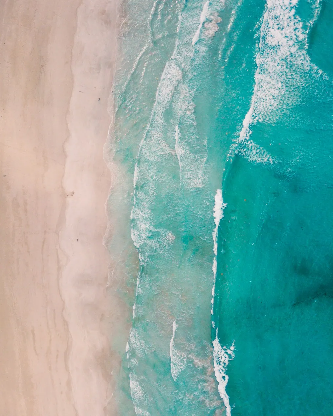 Surf breaking on a wide white-sand beach, seen from the air.